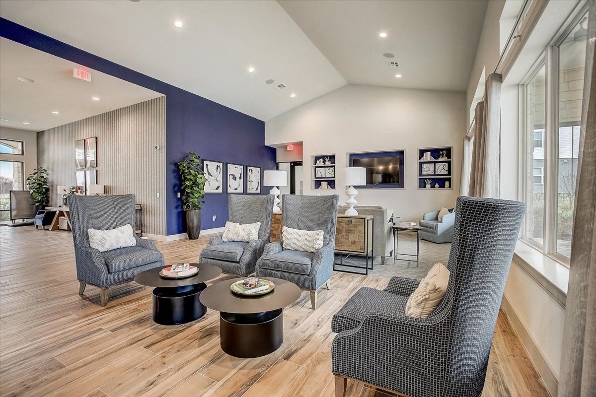 Clubhouse seating area with high-back chairs, small round tables, and sunlit windows along the wall.